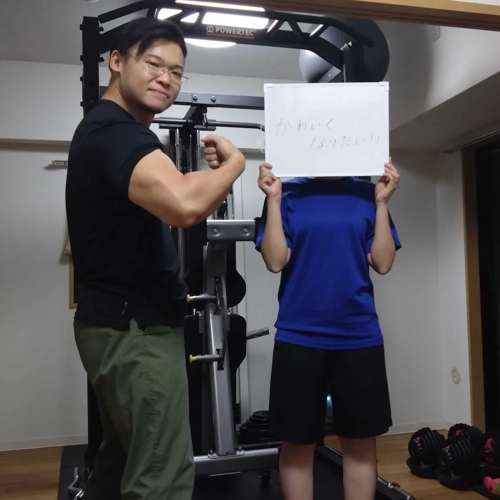 「かわいくなりたい!!」と書かれたホワイトボードを持つ会員さまと男性トレーナー｜パーソナルジムWORKOUTHOLIC横浜店